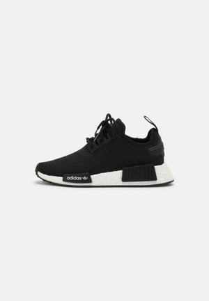 Czarny niski sneaker Adidas z białą wyściełaną podeszwą, czarnymi panelami bocznymi i sznurowadłami na jednolitym białym tle.