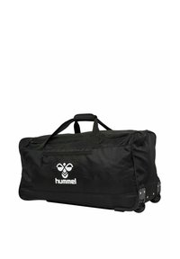 Czarna torba sportowa na kółkach wykonana z wytrzymałej tkaniny. Posiada dwa uchwyty, zasuwaną kieszeń oraz biały wzór logo na przedzie.
