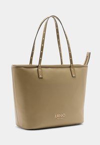 Bézs színű bőr válltáska két szegecselt fogóval, cipzáras részlettel és arany logóval az alján. Sima felületű, téglalap alakú, minimalista dizájn.