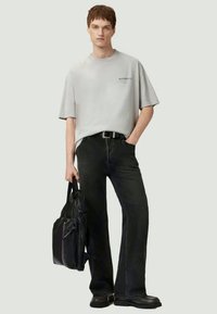 Γκρι oversized μπλούζα με λογότυπο, μαύρες ψηλόμεσες τζιν παντελόνες με ίσια πόδια και μια υφασμάτινη μαύρη σακίδιο. Απλά υποδήματα ολοκληρώνουν την εμφάνιση.