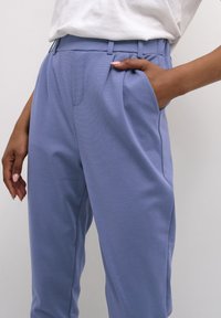 Lichtblauwe op maat gemaakte broek met plooien, een hoge taille en zijzakken. De stof heeft een soepele textuur.