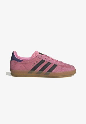 Sapatilha de camurça rosa com riscas pretas, sola de borracha, e calcanhar texturizado roxo. Apresenta um design de atacadores e uma marcação em relevo na lateral.