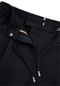 Marineblauwe broek met elastische tailleband, trekkoord, rits en knoopsluiting; slank stof met extra accentdetails bij de zakken.