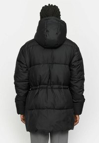 Fekete puff coat kapucnival, steppelt dizájnnal, megszorított derékkal és közép hosszú fazonnal. Az anyag fényesnek és simának tűnik.