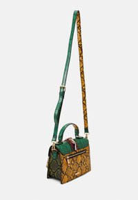 Torebka z wężowej skóry z zielono-żółtymi łuskami, złotymi elementami, górnym uchwytem oraz regulowanym paskiem z wzorzystym deseniem.