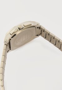 Αντρικό ρολόι χειρός από ανοξείδωτο ατσάλι με συνδεδεμένο λουράκι, πλευρικά κουμπιά και εγχάρακτη πίσω πλάκα που εμφανίζει την επωνυμία και τεχνικές λεπτομέρειες.