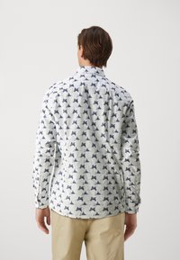 Koszula z długim rękawem wykonana z białej tkaniny z wzorem ciemnoniebieskich muszek, kołnierzyk typu point oraz zapięcie na guziki na mankietach.