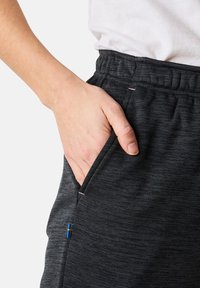 Svarta träningsbyxor med en texturerad väv; har en elastisk midja och en sidoficka. Liten blå och gul detalj nära fickan.