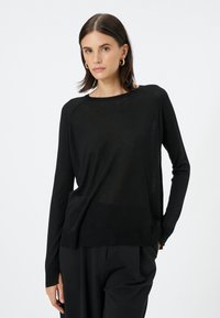 Musta pitkähihaisia neule, jossa on pyöreä kaula-aukko ja ribbireuna. Kevyt materiaali, joka on hieman väljä ja raglan-hihat.