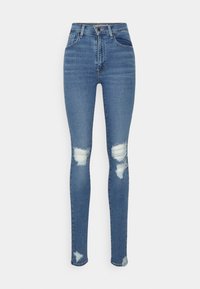 Pantalones vaqueros ajustados de mezclilla, con una cintura alta y parches desgastados en las rodillas con ligeras deshilachaduras. Diseño sencillo sin herrajes visibles.