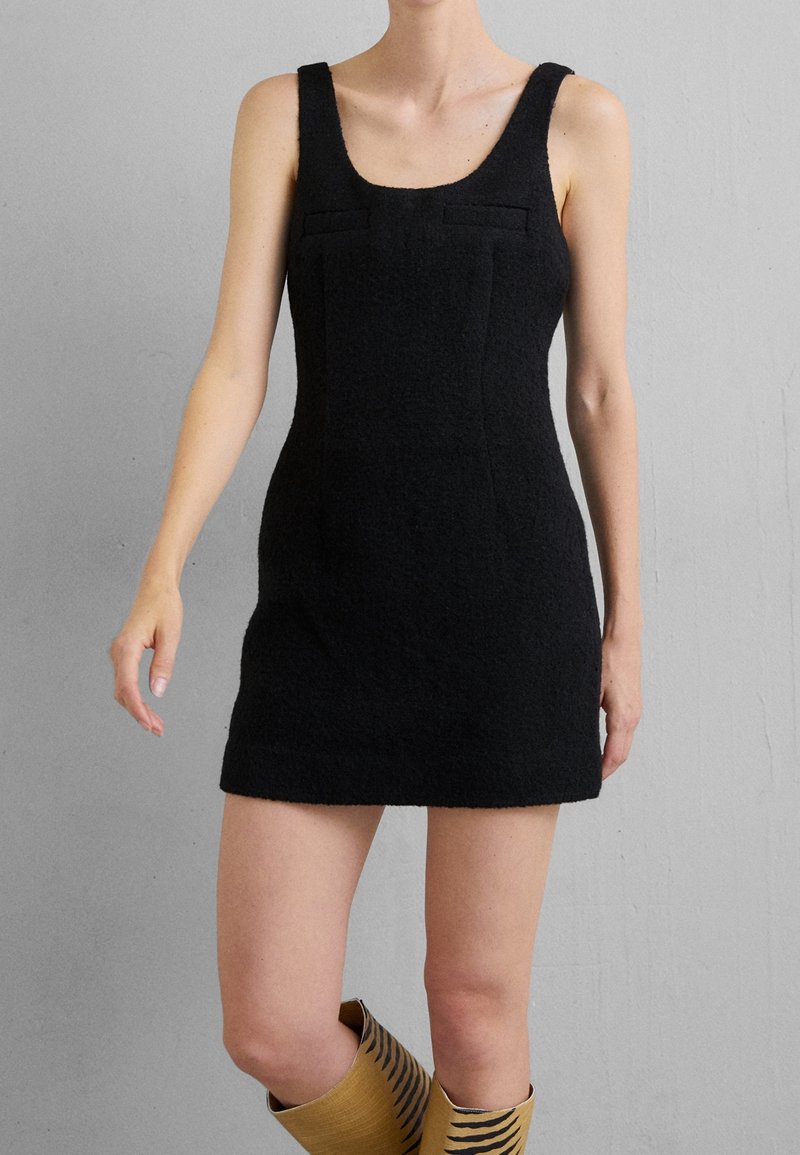 Schwarzes gestricktes Minikleid mit breiten Trägern, rundem Ausschnitt und vorderen Taschen. Figurbetontes Design und strukturierter Stoff, getragen mit gemusterten kniehohen Stiefeln.