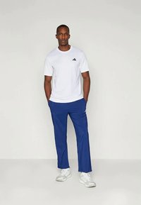 Balta trumpo rankovėmis marškinėliai su juodu logo, derinami su mėlynomis sportinėmis kelnėmis. Avalynė - baltos sportbačiai. Paprastas, kasdienis dizainas.