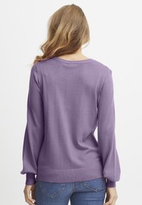 Svijetloplavi pulover s dugim rukavima, rebrastim manžetama i opuštenim krojem. Glatka tekstura i široki okrugli izrez. Opušteni dizajn.