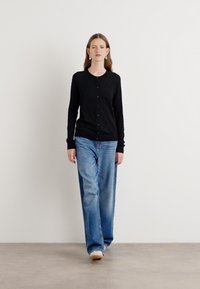 Svart knappet cardigan, lett stoff, slim fit. Båret med lyseblå, løstsittende jeans. Enkel design, minimalisme.