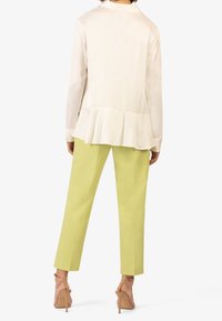 Blusa beige chiaro con orlo svasato, abbinata a pantaloni verdi chiari su misura. La modella indossa tacchi con strappi color nocciola per un look completo.