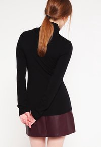 Zwarte lange mouwen top met een hoge kraag, gladde textuur en slank ontwerp, gecombineerd met een bordeaux leren minirok.