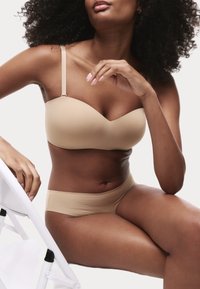 Soutien-gorge beige rembourré avec bretelles réglables et design sans coutures, associé à un slip de bikini assorti. Texture lisse et style minimaliste.