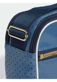 Borsa sintetica blu con superficie perforata, hardware dorato e una tracolla in tessuto blu. Presenta una cerniera dorata e dettagli in bianco a contrasto.