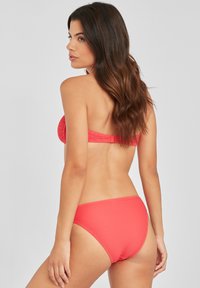 Koralfarbenes gestreiftes Bikini-Set mit Bandeau-Oberteil und mittelhohem Unterteil. Glatte Textur, minimales Zubehör und nahtloses Design.