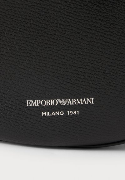 Μαύρη υφή δερμάτινης επιφάνειας με ασημί ανάγλυφο λογότυπο Emporio Armani και κείμενο "Milano 1981" κάτω από το λογότυπο.