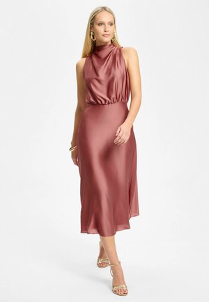 Femme portant une robe midi en satin sans manches couleur rose poudré avec un col montant, associée à des boucles d'oreilles créoles dorées et des talons à brides dorées.