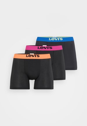 Boxers negros con una cintura azul que presenta un logo. El modelo está descalzo, mostrando el ajuste y diseño del producto.