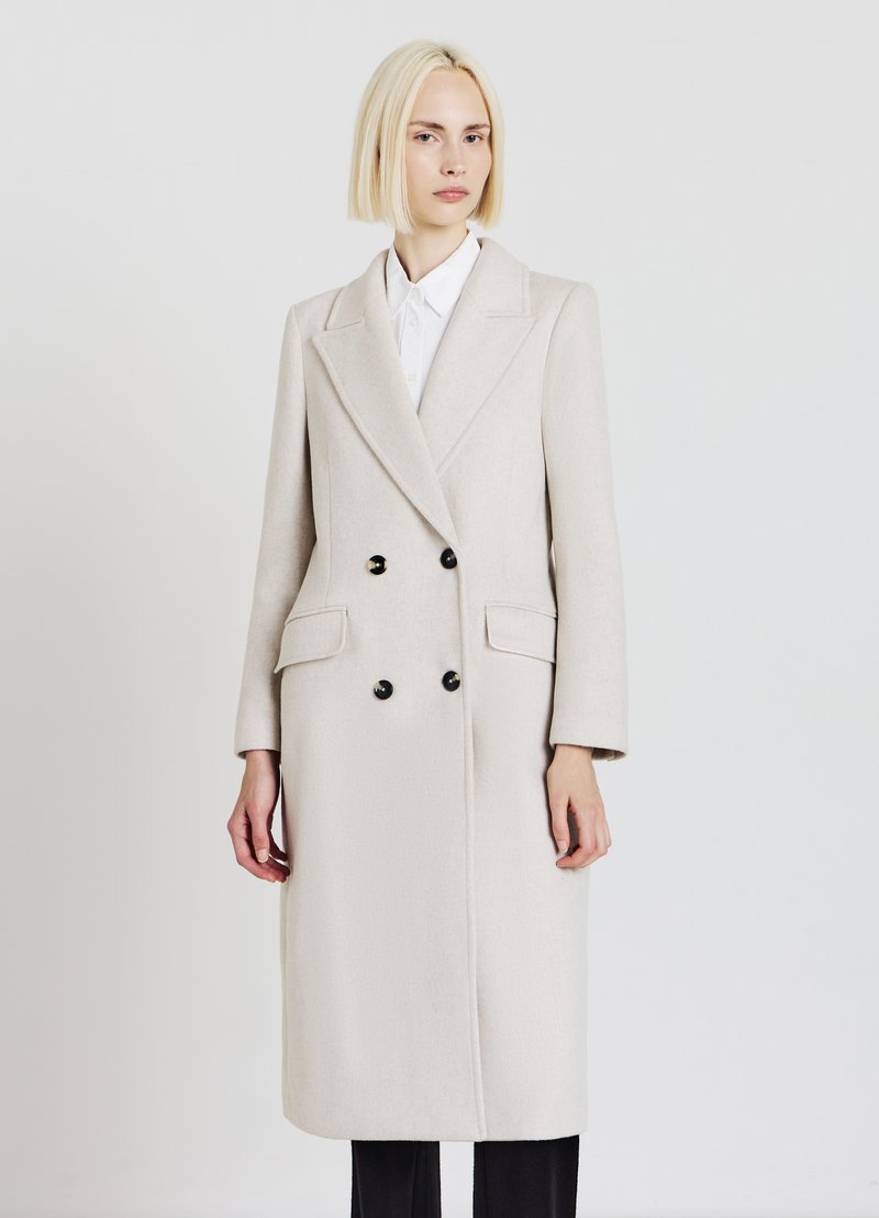 Cappotto doppio petto in lana beige chiaro con rever a lancia, dotato di due tasche frontali e bottoni neri. Maniche lunghe e taglio dritto.