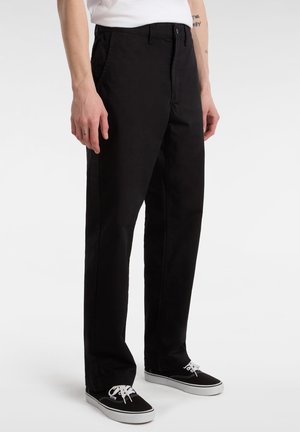 Pantaloni neri in cotone con vestibilità dritta, dotati di tasche laterali, chiusura con bottone e dettagli di cucitura discreti. Abbinati a sneakers nere.