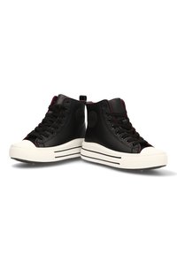 Par de zapatillas altas negras con suelas de goma blanca y rayas negras, cordones negros y un sutil detalle de ribete rojo.