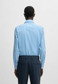 Camicia a righe blu chiaro con colletto aperto e polsini con bottoni, abbinata a pantaloni scuri blu con trama e vita elastica.