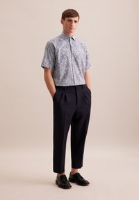 Koszula z krótkim rękawem w jasnoniebieski wzór paisley, z kołnierzykiem, połączona z ciemnymi granatowymi spodniami z zakładkami i czarnymi butami oxford. Prosta tekstura i design.