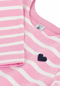 Rosa-weiß gestreiftes Baumwollhemd mit rundem Ausschnitt, versehen mit einem kleinen marineblauen Herzdetail. Weiche Textur und leichter Stoff.