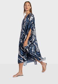 Kaftan fluide en bleu marine et blanc, avec un motif abstrait audacieux, un col en V et des manches larges. Porté avec des sandales argentées à brides.