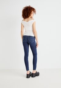 Vitt, figurnära off-shoulder topp i kombination med mörkblå skinny jeans och svarta plattformsträskor; har bakfickor och sömdetaljer.