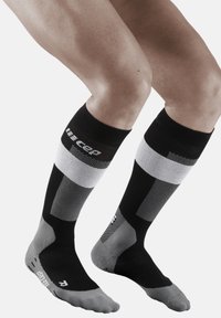Calze a compressione in nero, grigio e bianco con motivi geometrici. Presentano un tallone e una punta rinforzati. Altezza fino al polpaccio con dettagli del logo.