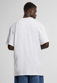 White cotton t-shirt with short sleeves, a relaxed fit, and a round neckline, shown from the back, paired with blue denim shorts.