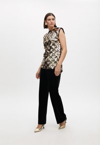Sequined top with a dark base, featuring metallic circular embellishments. Worn with black velvet pants and gold pointed heels.
