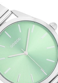 Montre en acier inoxydable argentée avec un cadran en vert menthe brossé. Présente des index horaires fins en argent et des aiguilles minimalistes. Nom de la marque "oozoo" affiché.