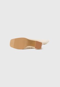 Bottine beige posée sur le côté, montrant une semelle à bout carré et un talon bloc avec des sections de grip texturées.