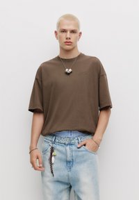 Hnědé oversized tričko s krátkým rukávem a kulatým výstřihem, spárované se světle modrými džínami s výdrží, které mají pruhovaný pas a klíčenku.