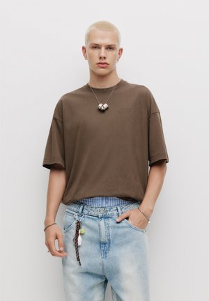 Brun oversized kortærmet t-shirt med rund hals, parret med lyseblå slidte denimjeans med stribet talje og nøglering.