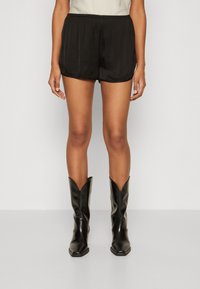 Black satin shorts with an elastic waistband, featuring a relaxed fit and smooth texture, paired with knee-high black leather boots.