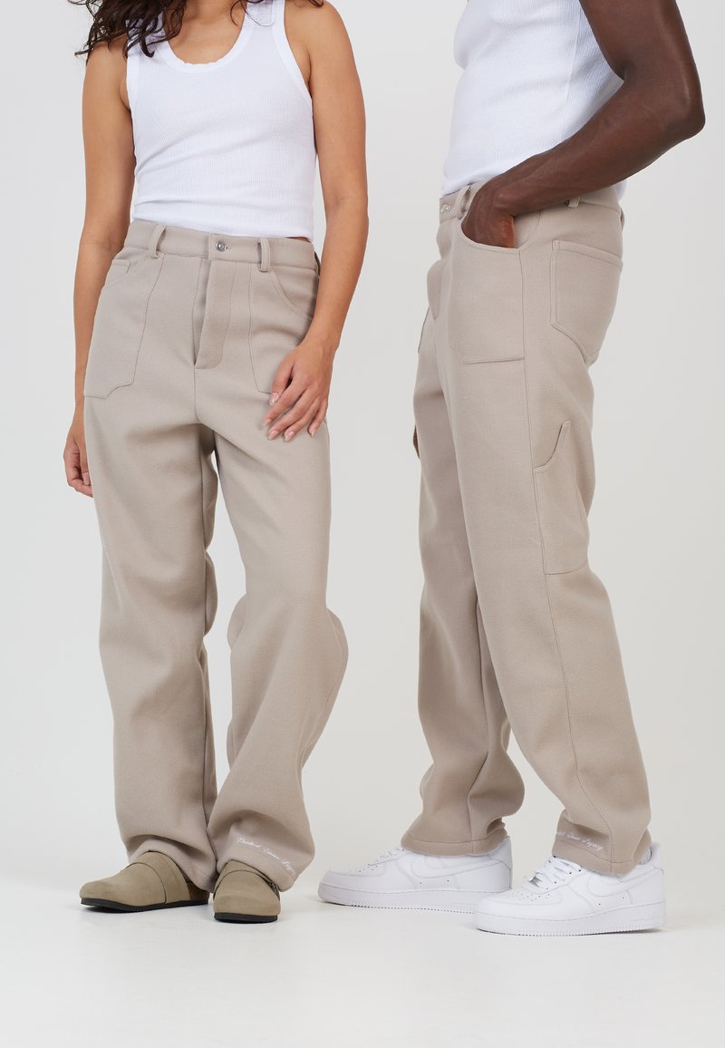 Pantaloni bej cu croi larg, cu o textură netedă, talie înaltă și buzunare. Purtați cu un top alb fără mâneci și saboți bej, asortați cu adidași albi.