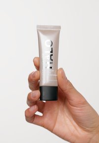 Hydratant teinté Smashbox Halo dans un tube argenté et noir, au design élégant et à la texture lisse, tenu dans une main.