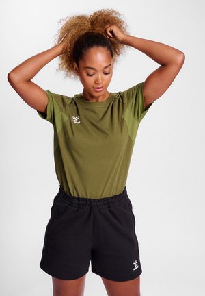 Groene T-shirt met korte mouwen en logo op de linkerborst, gecombineerd met zwarte shorts met elastische tailleband. De stoffen lijken zacht en casual.