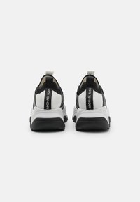 Zapatillas deportivas en blanco y negro con parte superior de malla, entresuela blanca gruesa, suela de goma negra y tirador trasero con la marca "Michael Kors".