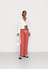 Red linen pants with a drawstring waist, paired with a white cropped top and a light denim jacket. Accessories include a small white handbag and sandals.