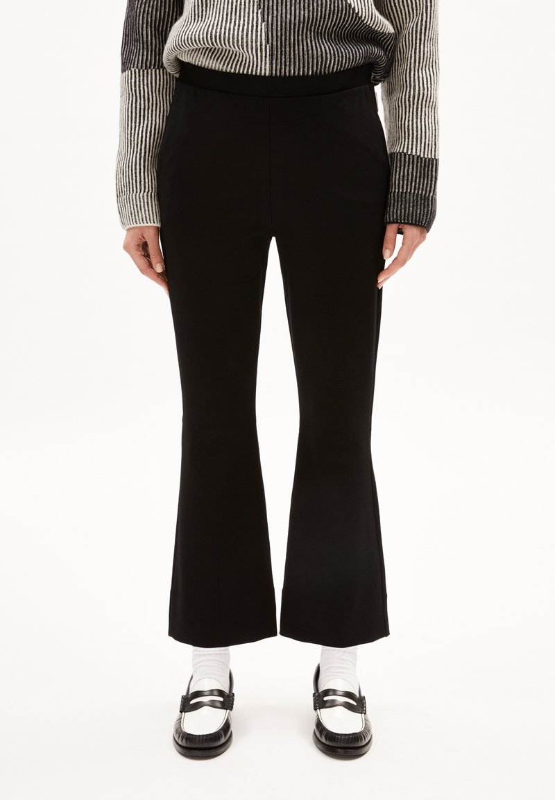 Zwarte flared broeken met een gladde textuur en een elastische tailleband, gecombineerd met pronerende zwart-witte loafers en witte sokken.