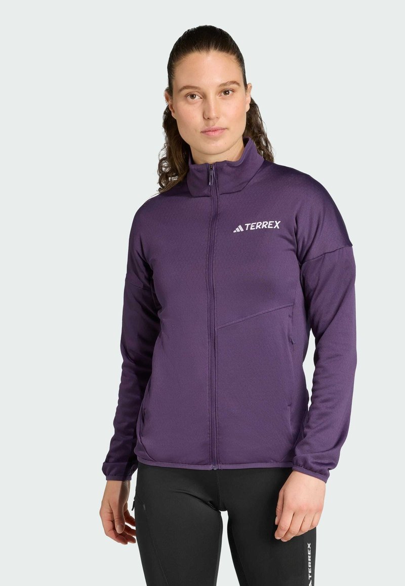 Giacca Terrex viola con colletto alto, zip frontale, tasche laterali e texture liscia, abbinata a leggings neri.
