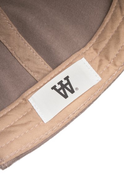 Tissu marron avec des coutures beige et une étiquette blanche affichant un logo noir. La texture est lisse avec un léger éclat.